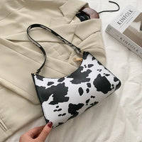 Compacte dames schoudertas met zwart-witte koeprint en rits