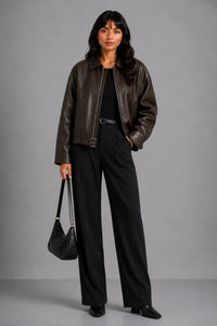 Vrouw draagt donkerbruine oversized dames jas met leren look open over zwarte top en zwarte wijde pantalon