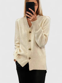 Vrouw in beige gebreid vest met goudkleurige hartvormige knopen