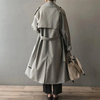 Achterzijde van grijze lange dames trenchcoat met ceintuur