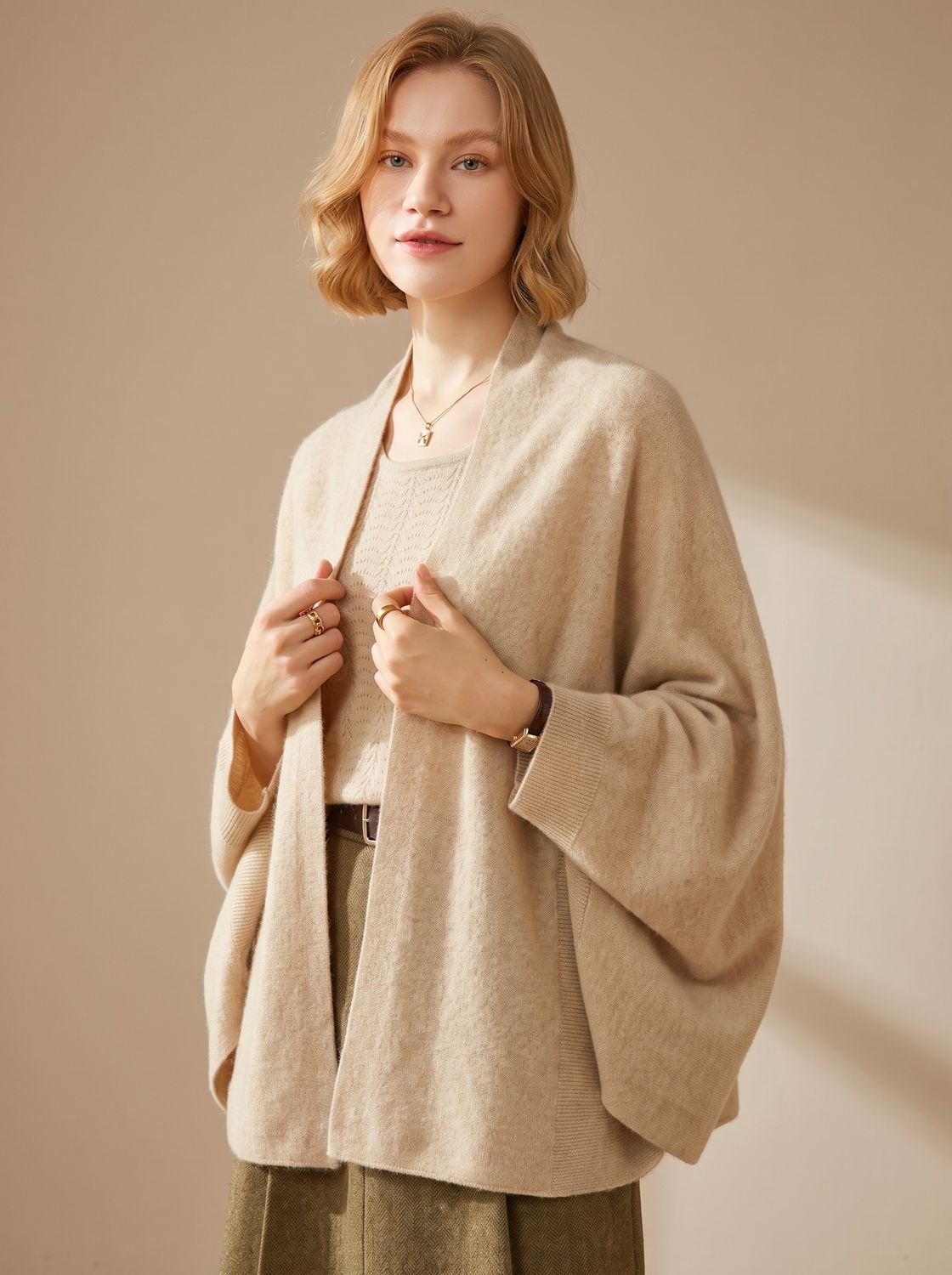 Vrouw draagt oversized poncho sjaal met armgaten in beige over een top