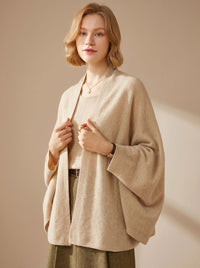 Vrouw draagt oversized poncho sjaal met armgaten in beige over een top