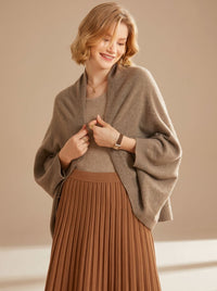 Vrouw draagt oversized poncho sjaal met armgaten in taupe over een top