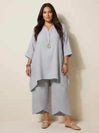 Vrouw in lichtgrijze tweedelige set met lange asymmetrische tuniek en losse broek, vooraanzicht