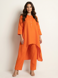 Vrouw in oranje tweedelige set met lange asymmetrische tuniek en losse broek, vooraanzicht