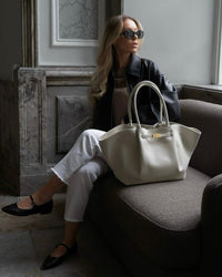Crème oversized schoudertas met goudkleurige sluiting op een bank
